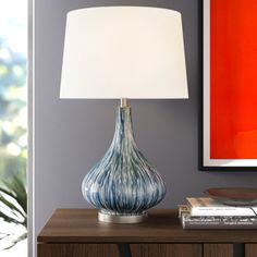 a blue and white lamp sitting on top of a wooden table next to a painting