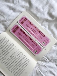 two pink tickets sitting on top of an open book next to a white bed sheet