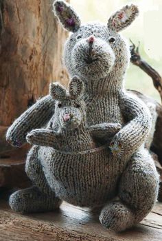 two knitted rabbits sitting next to each other on top of a wooden table in front of a window