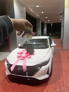 a person is holding a key to a white car with pink ribbon on the hood