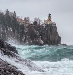 a lighthouse on top of a rocky cliff in the ocean with waves crashing around it