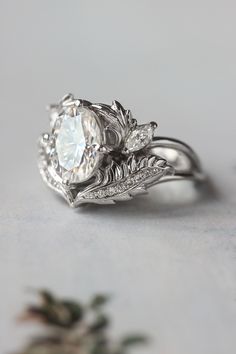 a close up view of a diamond ring on a white surface with flowers in the background