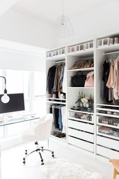 a white closet filled with lots of clothes next to a desk and chair in front of a window