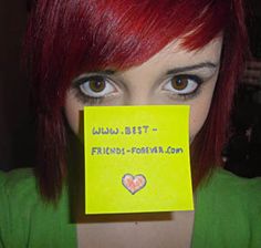 a woman with red hair and green shirt holding up a yellow post - it note