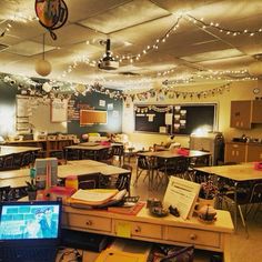 an empty classroom with desks and laptop on the floor, lights strung from the ceiling