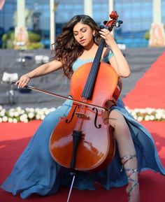 a woman in a blue dress is playing the cello on a red carpeted area