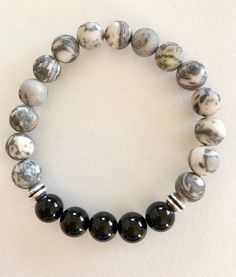 "Natural matte grey Picasso jasper and polished black onyx gemstones on a stretch bracelet. Men's handsome stretch bracelet of 10mm matte grey and white Picasso jasper and 10mm polished black onyx gemstones. Silver pewter wheel spacers add extra accents Bracelet is made to order on professional stretch elastic. When selecting size please add 3/4\" to 1\" to actual wrist measurement for a comfortable fit. Handsome bracelet for everyday wear!" Casual Black Stretch Bracelet With Gemstone Beads, Adjustable Black Agate Stretch Bracelet, Casual Black Agate Beaded Bracelets, Paris Charm Bracelet, Black Onyx Bracelet, Surfer Necklace, Wood Bead Necklace, Picasso Jasper, Jasper Bracelet