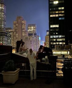 three men standing on top of a roof in front of tall buildings at night time