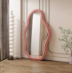 a pink mirror sitting on top of a wooden floor next to a vase and plant