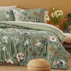 a bed with green and white flowers on it in a room next to a wicker basket