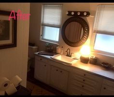 a bathroom sink under a round mirror next to a window with light coming through it