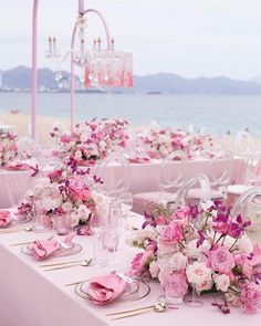 the table is set with pink flowers and place settings for an elegant dinner on the beach