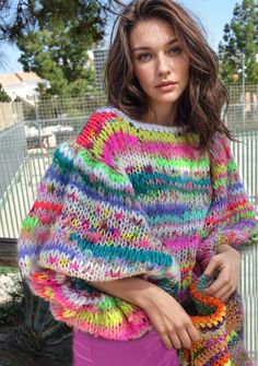 a woman wearing a multicolored knitted sweater and holding a purse in her hands