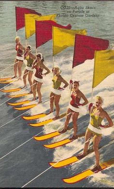 a group of women standing on surfboards in front of yellow and red flag poles