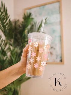 a person holding up a plastic cup with straws in it and flowers on the side