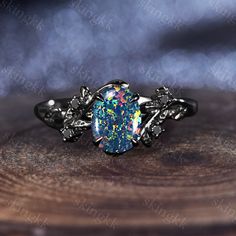 a ring with an oval shaped blue opal surrounded by leaves on top of a piece of wood