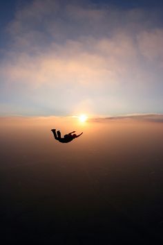 a person is flying in the sky at sunset or dawn with their arms spread out