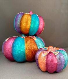 three brightly colored pumpkins sitting next to each other on top of a gray surface