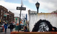 people are walking down the street in front of a graffiti covered wall with a man's face painted on it