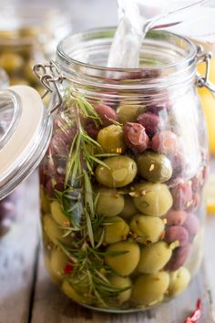 a jar filled with olives and rosemary sprigs on top of a wooden table