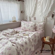 a white bed with pink flowers on it in a bedroom next to a small table