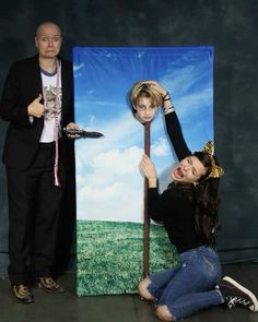 two people standing next to each other with a painting on the wall behind them and one holding a stick