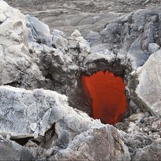 a hole in the rocks that is filled with red liquid or water and surrounded by large rocks