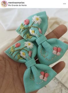 a hand is holding a small blue bow with flowers on the front and back of it