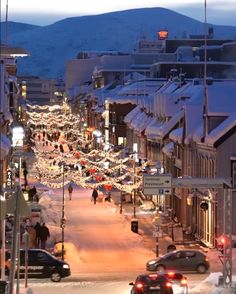 a city street with cars parked on the side of it and christmas lights hanging from the buildings