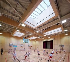 a group of kids playing basketball inside of a gym building with skylights overhead and people on the court