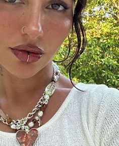 a close up of a person wearing a necklace and nose piercings with trees in the background