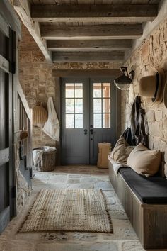 an entryway with stone walls and wooden flooring is decorated in neutral tones, along with several hats hanging on the wall