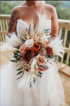 a woman in a wedding dress holding a bridal bouquet with feathers and flowers on it