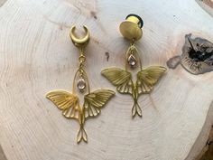 two gold earrings with butterfly wings hanging from them on top of a piece of wood