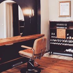 a chair and mirror in a room with wood flooring on the ground, next to a shelf full of bottles