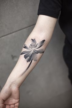 a black and white flower tattoo on the left arm, with watercolor style petals