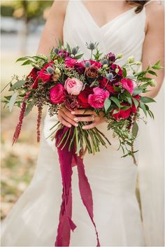 a bride holding a bouquet of red and pink flowers on her wedding day at the park