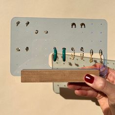 a person is holding a wooden board with rings on it and an earring holder in front of them