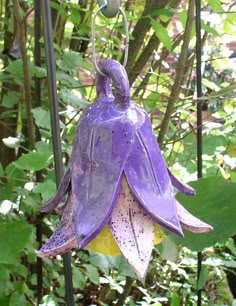 a purple flower hanging from a metal pole in the middle of some trees and bushes