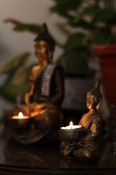 two buddha statues sitting next to each other on a table with candles in front of them