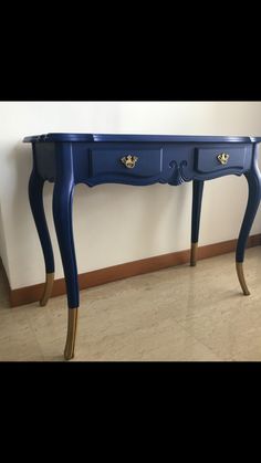 a blue table with two drawers and gold handles on it, against a white wall