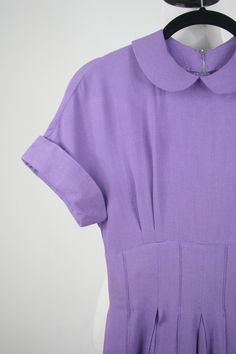 "1950s hand made dress. Purple rayon, plain weave fabric. The weight of the fabric would make a great swing dress. Peter Pan collar and cuffed cap sleeves. Wide, 3\" waist. Waist, collar, and cuffs have stiffening in them. Full skirt is box pleated and has reverse, decorative seaming. (see next to last photo although the color is off in this photo) 3.5\" hem. Fastens in the back with a short metal zipper and another one in the side. Freshly laundered. Excellent condition. There is one small dark 1950s Style Short Sleeve Lined Dress, 1950s Style Lined Short Sleeve Dresses, 1950s Style Vintage Dress With Short Sleeves, 1950s Style Vintage Short Sleeve Dress For Work, Fitted Dresses With Peter Pan Collar For Vintage Fashion, 1950s Style Vintage Dress With Short Sleeves For Daywear, Retro Vintage Short Sleeve Dress For Work, Retro Short Sleeve Vintage Dress For Work, Lined Cotton Vintage Short Sleeve Dress