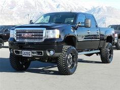 a large black truck parked in a parking lot next to other trucks and snow covered mountains