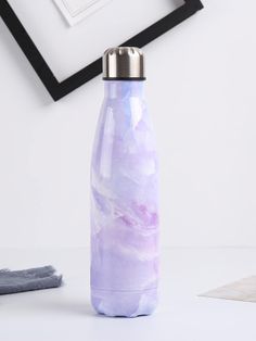 a purple marbled water bottle sitting on top of a white table next to pictures