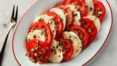 sliced tomatoes and mozzarella on a white plate with silverware next to it