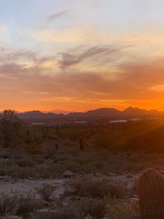 the sun is setting in the desert with mountains and cactuses on the ground below