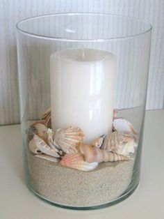 a candle that is sitting in some sand with shells on the ground next to it