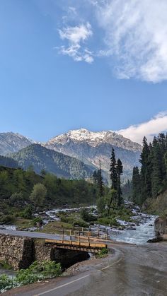 a small bridge over a river with mountains in the background