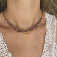 a woman wearing a brown necklace with gold beads and a medallion on the front of her neck