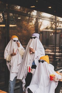 two people dressed in white and yellow are walking down the street while holding cups with drinks